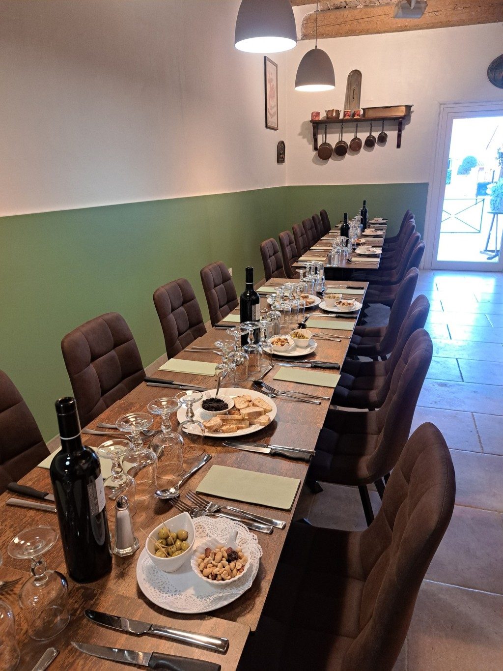 La salle du restaurant : de longues tables dressées pour un grand repas, murs verts et bois